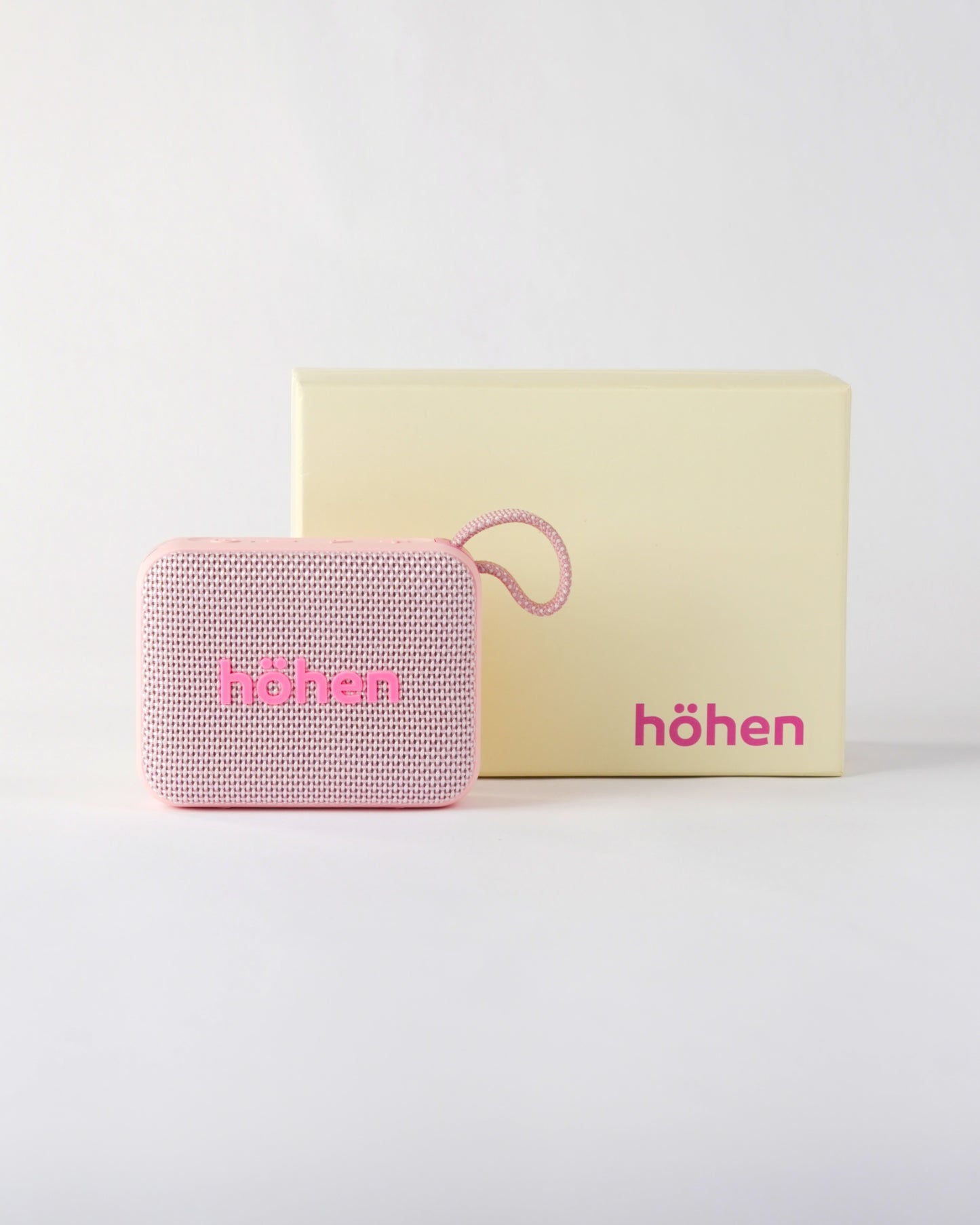 The pink höhen move bluetooth speaker presented next to its premium minimalist cream-colored branded packaging box