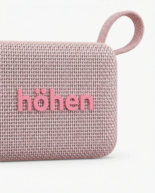 Parlante Bluetooth Höhen Move color rosa con acabado en tela, diseño compacto y correa de transporte.
