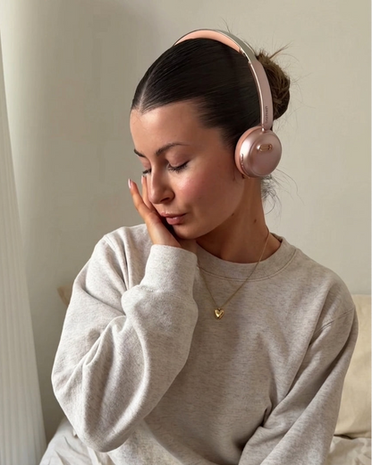 A portrait of a woman wearing the rose gold höhen Aura Mini wireless headphones, reflecting a moment of calm and sophisticated technology use