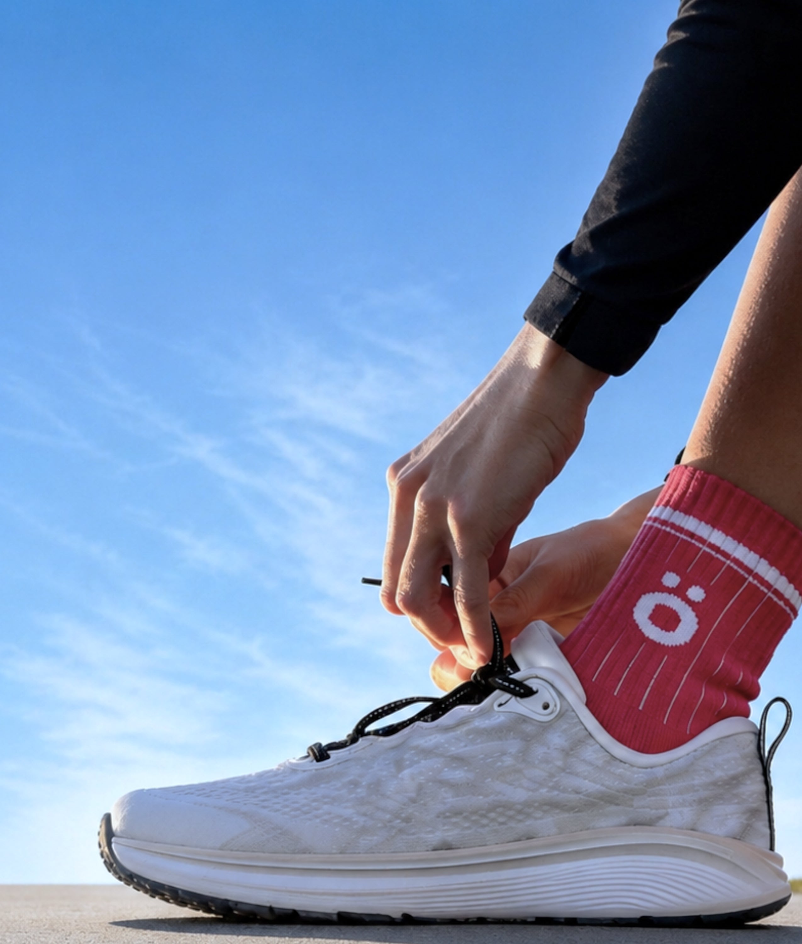 Close-up of a person tying white running shoes while wearing magenta höhen Core Merino socks outdoors under a clear blue sky