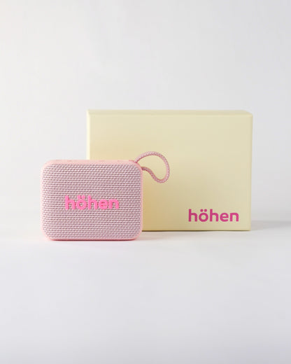 The pink höhen move bluetooth speaker presented next to its premium minimalist cream-colored branded packaging box
