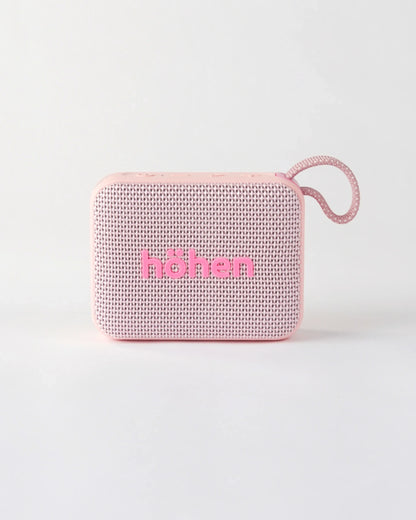 Front view of the compact höhen move portable bluetooth speaker in pale pink with a woven fabric grille and carrying loop