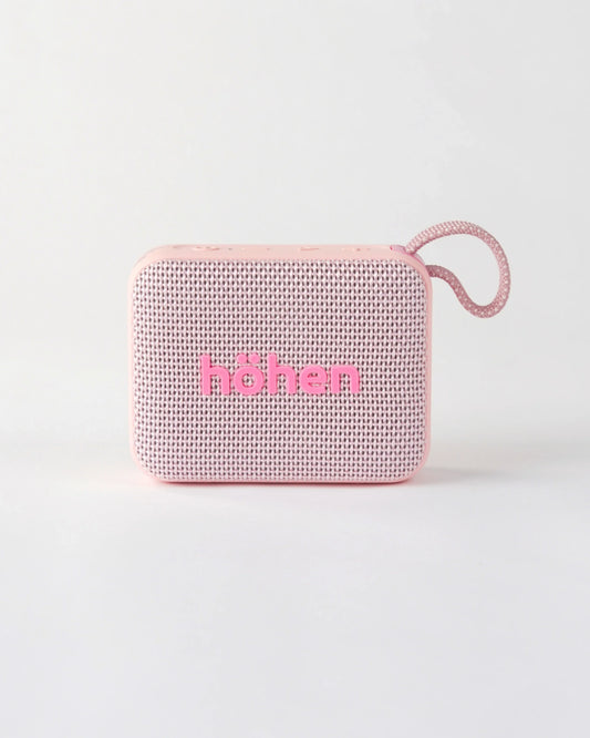 Front view of the compact höhen move portable bluetooth speaker in pale pink with a woven fabric grille and carrying loop