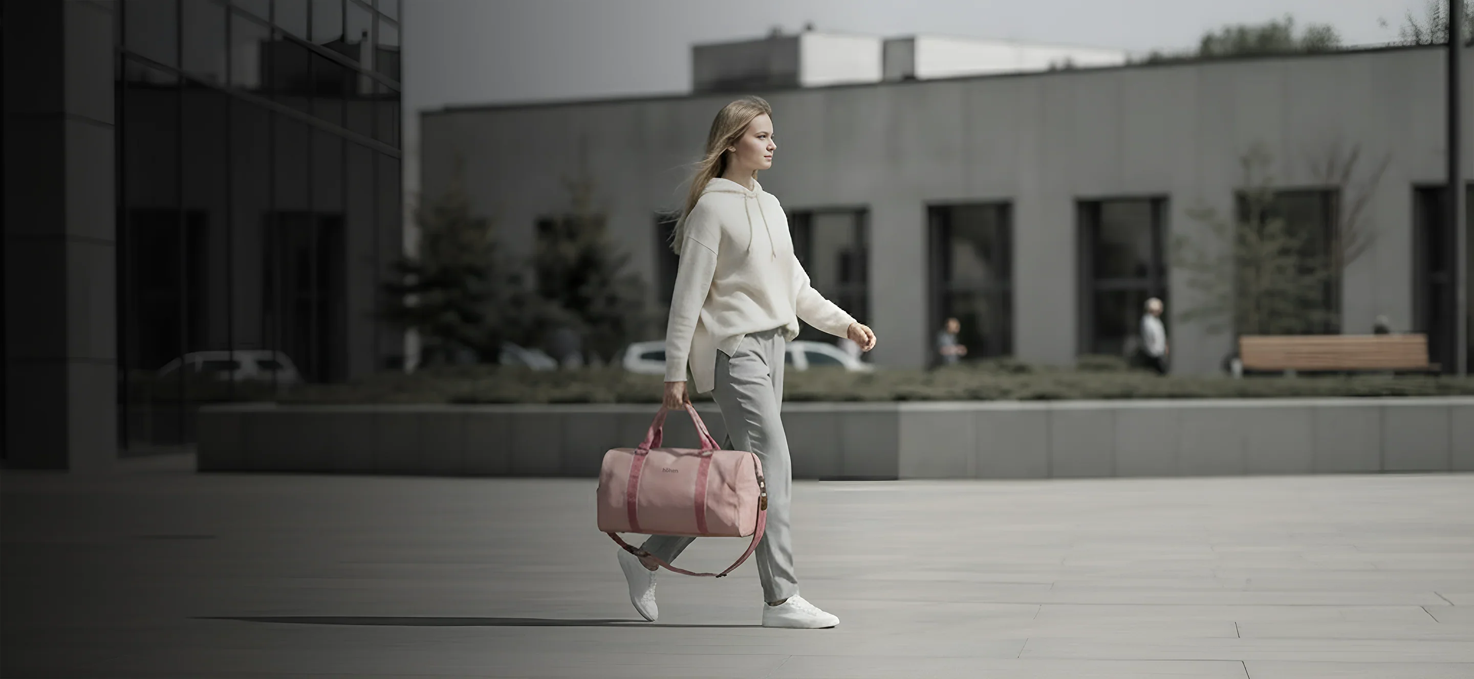 Woman walking through the city carrying the höhen one duffel bag in pink, perfect for an active urban lifestyle.