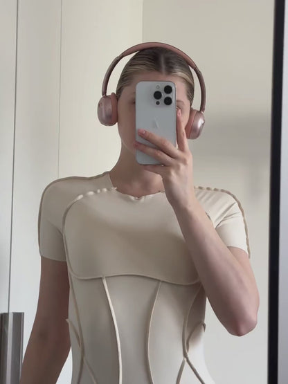 A woman wearing pink höhen aura mini wireless headphones during a workout session, showing a mirror selfie and the back detail of the headphones with a sleek bun hairstyle.
